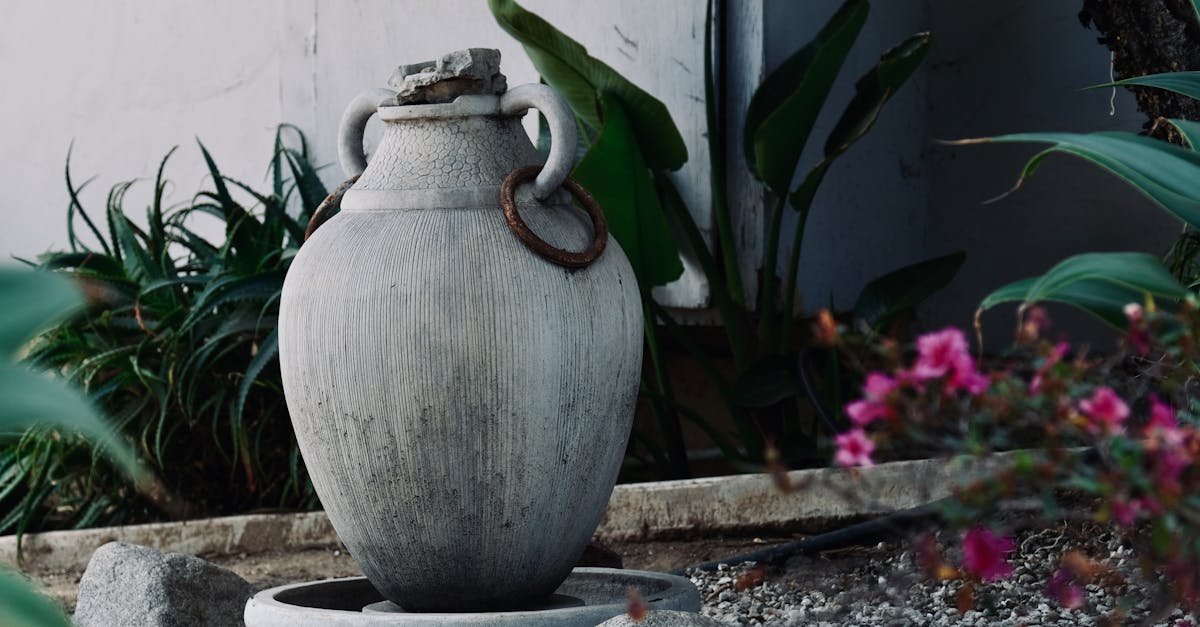 A large stone vase serves as a focal point in a serene garden, surrounded by greenery and flowers.